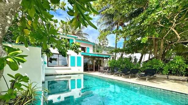 A swimming pool with clear blue water, surrounded by lush greenery and a building with a white facade and teal accents. - Villa Goodwill Beach House 3bedrooms on Beach front & private pool Patong Phuket (Tambon Patong)
