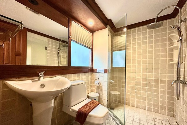 Baño con lavamanos blanco, inodoro y ducha con mampara de vidrio.