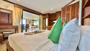 A hotel room with a large bed, a desk, and a chair. There is a window with curtains, a wooden wardrobe, and a door leading to another room. - Villa Goodwill Beach House 3bedrooms on Beach front & private pool Patong Phuket (Tambon Patong)