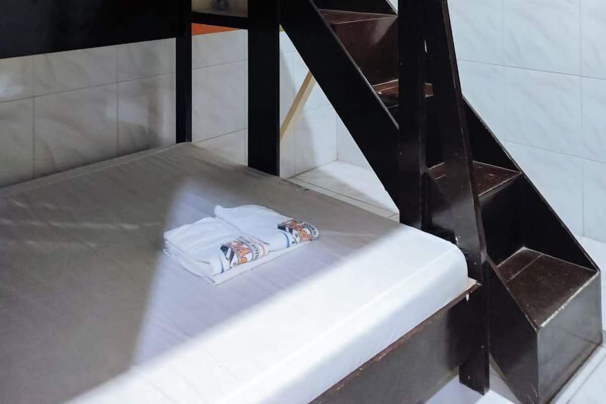 Un lit avec un drap blanc et une serviette pliée, un escalier en bois sombre et des murs recouverts de carreaux blancs.