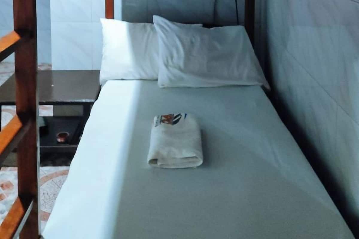 Un lit simple avec un matelas et des oreillers blancs, une petite table avec une tasse et une chaise en bois.