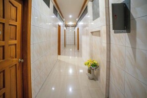 A hallway with a wooden door, a vase with flowers, and a wall-mounted device. - RedDoorz @ Pvc Pension Haus (Tagum)