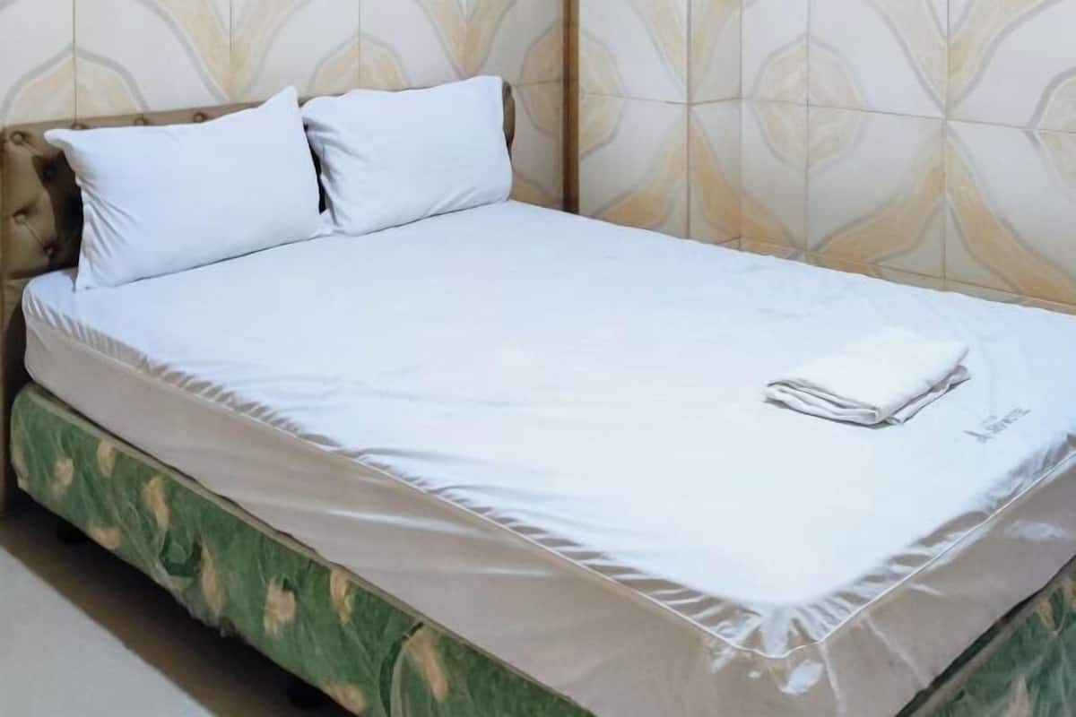 Un lit bien fait, avec du linge de lit blanc et une serviette pliée posée sur le côté.