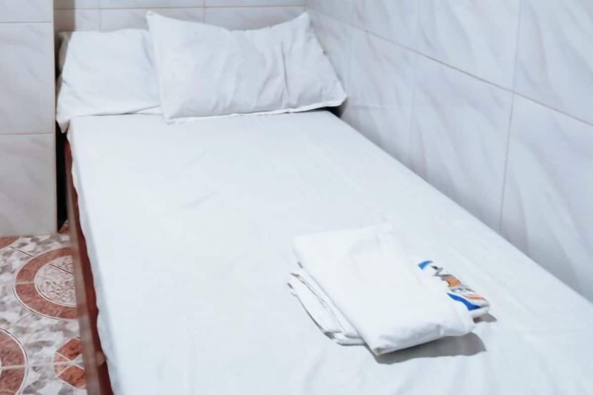 Un lit simple avec une literie et des oreillers blancs, une serviette pliée et un magazine posés sur le lit.