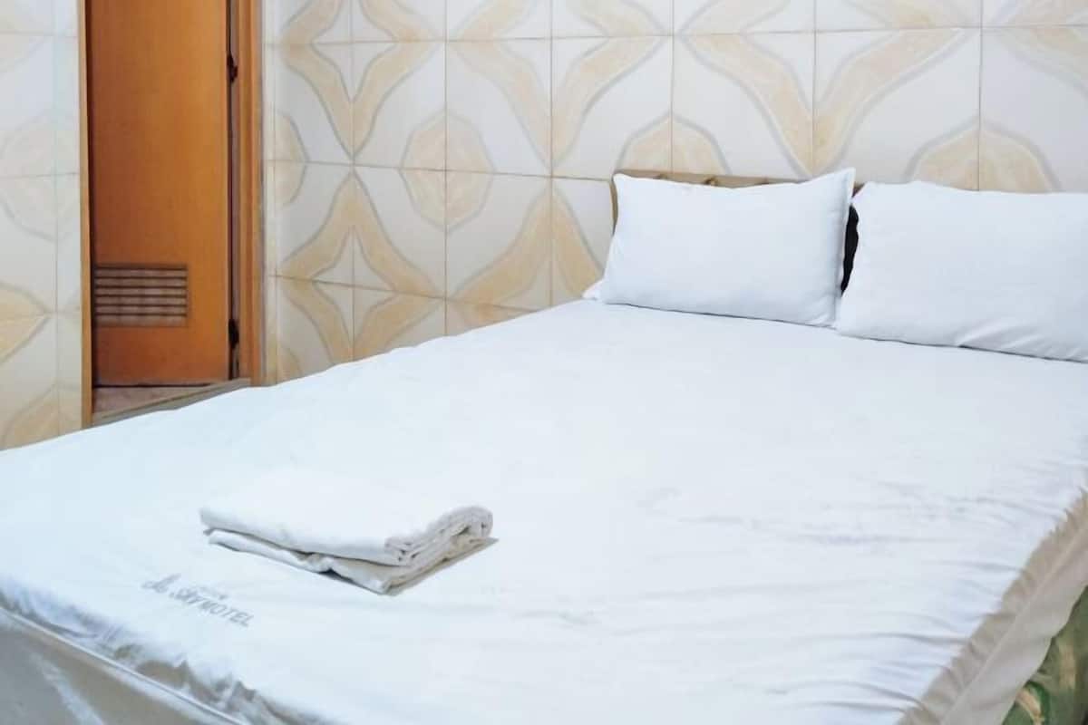 Un lit bien fait, avec du linge de lit blanc et des oreillers, une serviette pliée, et un mur à motifs en arrière-plan.
