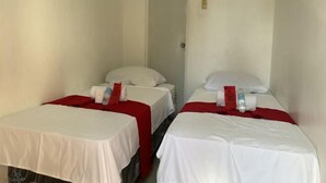 Deux lits simples, avec du linge de lit blanc et des couvre-lits rouges, dans une chambre étroite aux murs blancs.