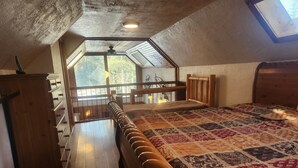 Une chambre à coucher avec un lit en bois, une courtepointe, une commode en bois et une lucarne.