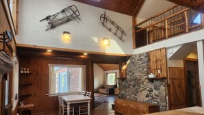 Un vaste espace de vie aménagé dans un style loft, avec une cheminée en pierre, des poutres apparentes et une table à manger avec des chaises.