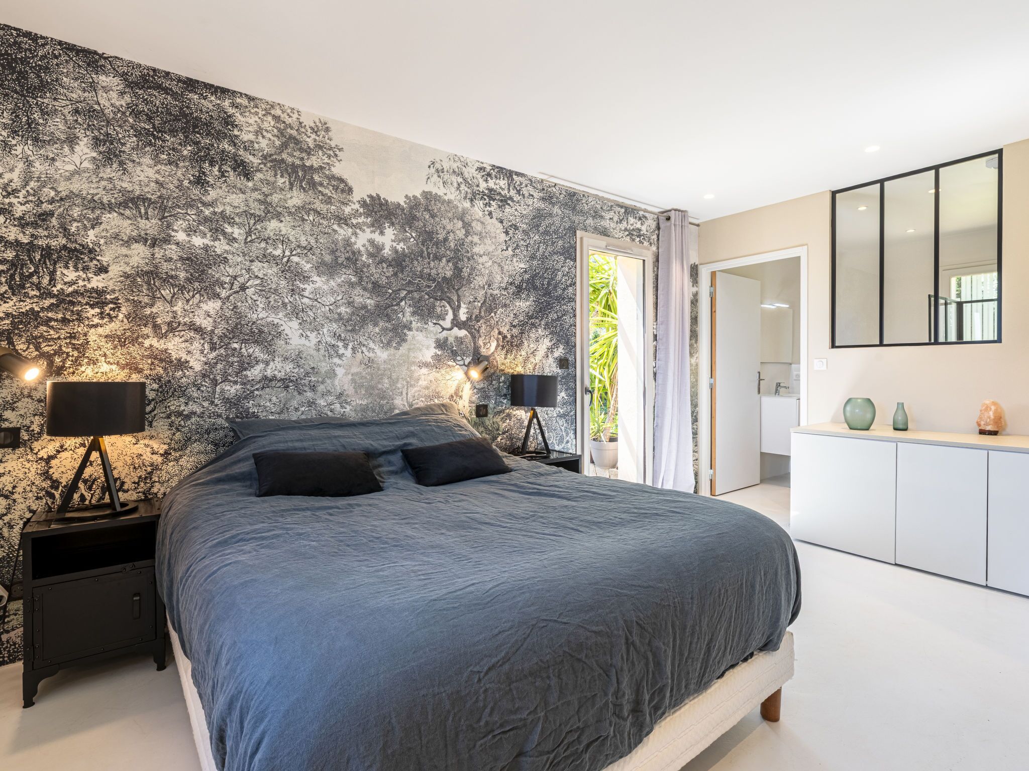 Une chambre à coucher avec un grand lit, deux tables de chevet avec des lampes, une armoire et une salle de bain visible à travers une porte ouverte.
