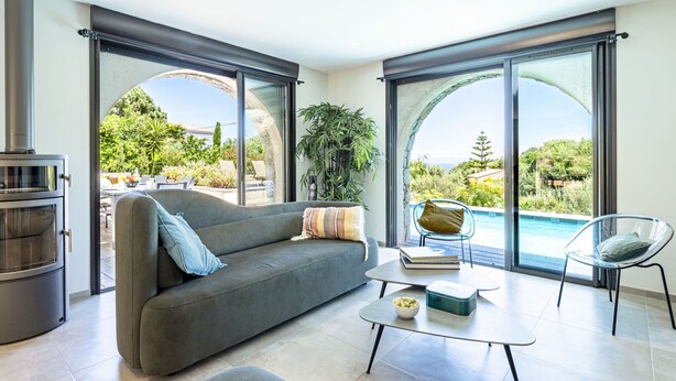 A modern living room with a sofa, coffee table, and a view of a swimming pool and greenery.