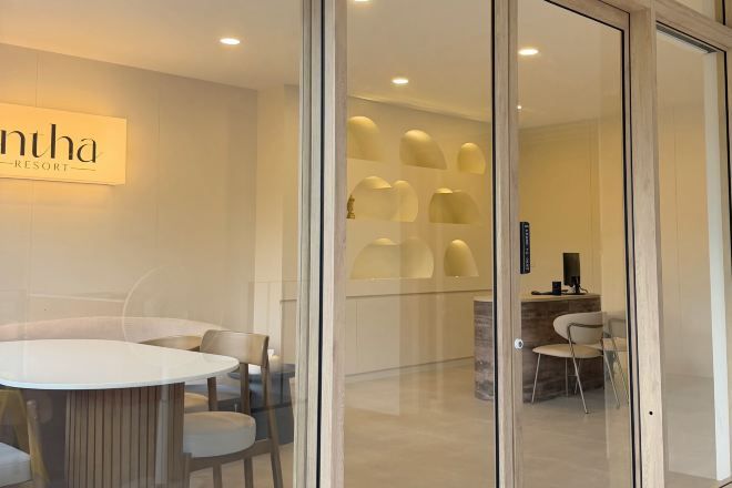 A modern interior with a glass partition, a round table, and chairs, and a sign that reads 'nhã RESORT'.