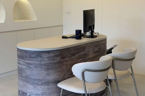 A reception area with a curved counter, a flat-screen TV, a coffee machine, and two white chairs. - Intha Resort (Pak Tho)