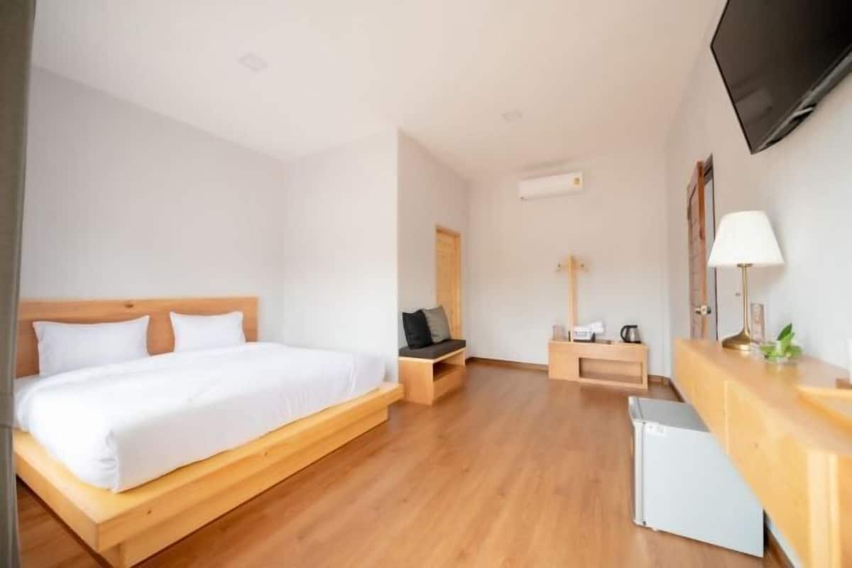 A hotel room with a wooden bed, a small seating area, a desk with a lamp, and a TV mounted on the wall.
