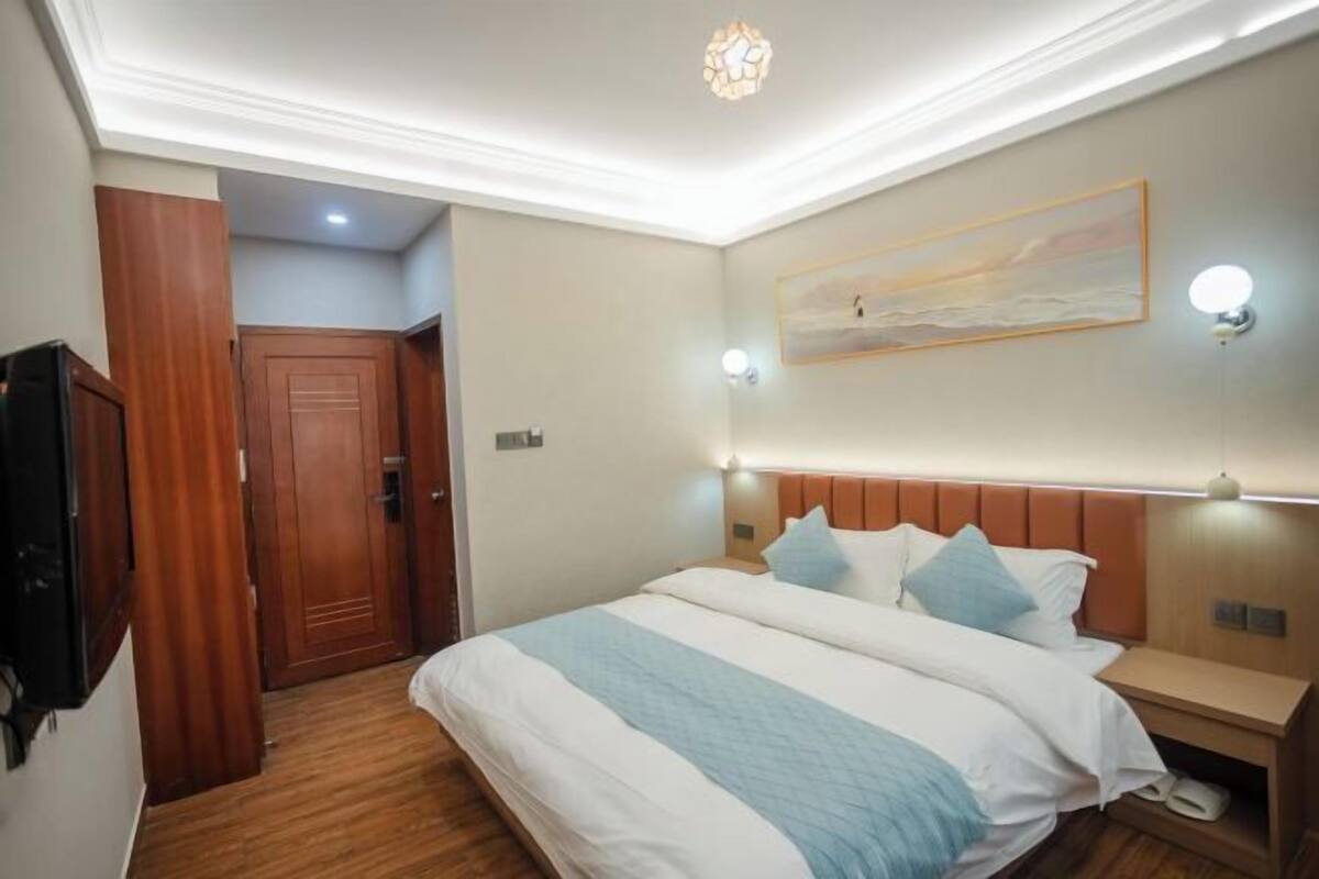 Hotellihuone, jossa on suuri sänky, puinen pääty, yöpöydät ja taulu seinällä.