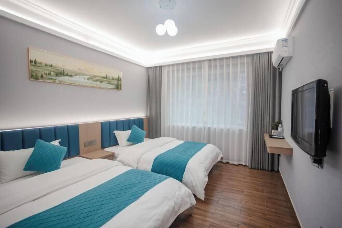 Hotellihuone, jossa on kaksi sänkyä, seinällä taulu, televisio ja ikkuna, jossa on verhot.