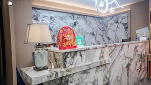 Een hotel receptiebalie met een marmeren aanrecht, een lamp en een decoratief bord met rode en groene accenten.