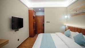 Een hotelkamer met een bed, een aan de muur bevestigde televisie, een houten deur en een schilderij.