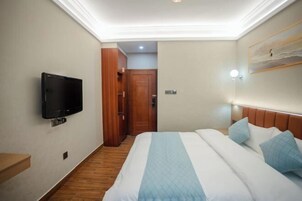 Una habitación de hotel con una cama, un televisor montado en la pared, una puerta de madera y un cuadro.