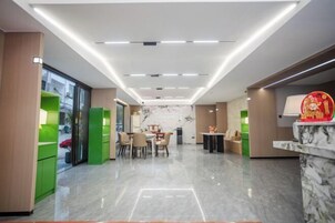Un moderno vestíbulo de hotel con una recepción de mármol, zonas de estar verdes y un comedor con mesas y sillas.