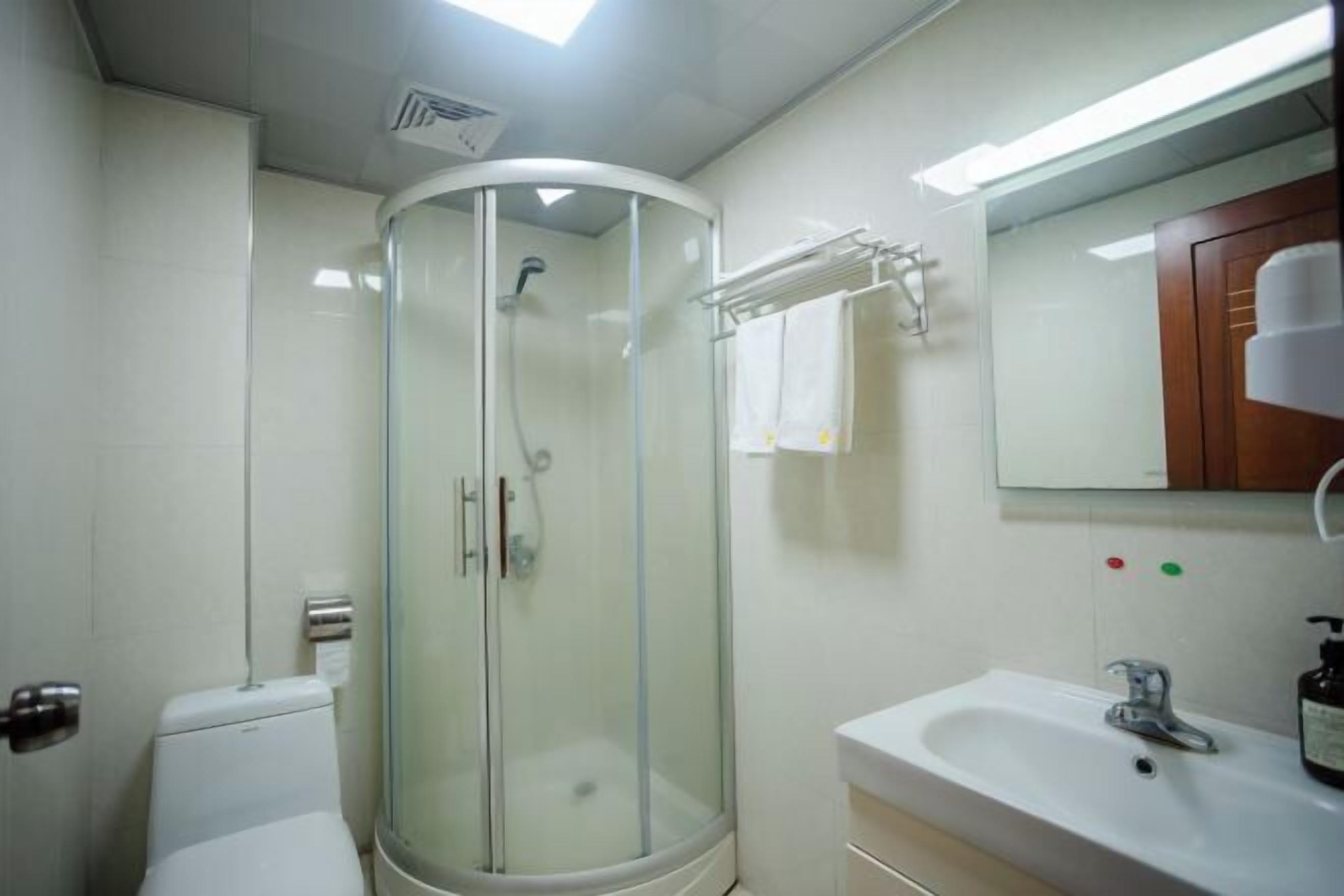 Une salle de bain avec une douche à parois de verre, un lavabo blanc et un miroir surmonté d’un meuble en bois.