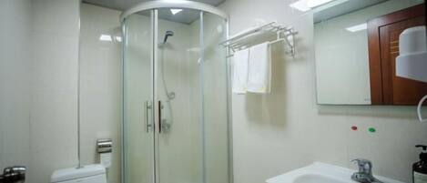 Une salle de bain avec une douche à parois de verre, un lavabo blanc et un miroir surmonté d’un meuble en bois.