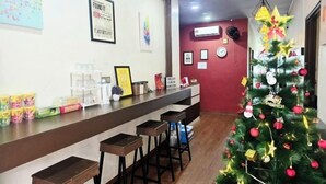 A reception area with a counter, bar stools, a Christmas tree, and various framed items on the wall. - Cow B Homestay Semporna (Semporna)