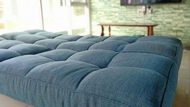 A tufted sofa in a room with a stone wall and a flat-screen TV mounted above it. - Cow B Homestay Semporna (Semporna)