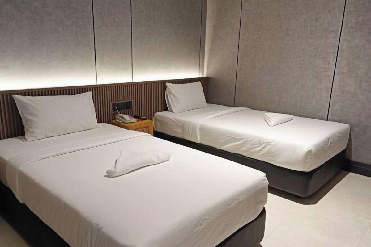 A hotel room with two single beds, a bedside table with a phone, and a wall-mounted light fixture.