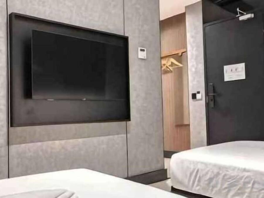 A hotel room with a flat-screen TV mounted on the wall, a bed with white bedding, and a dark door with a sign.
