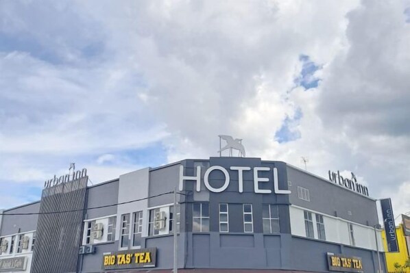 Een hotel met een moderne gevel, een opvallend 'HOTEL'-bord en een 'BIG TASTE TEA'-winkel op de begane grond.