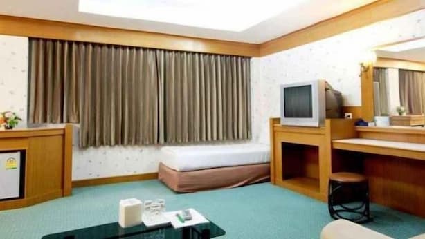 A hotel room with a bed, a desk, a television, a mirror, and a small stool. - River Hotel The Budget (Nakhon Pathom)