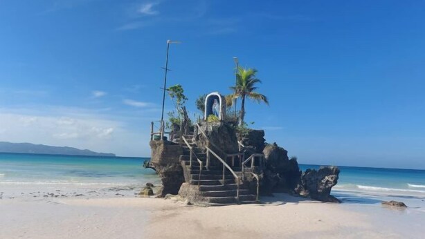 A rock formation with a staircase leading to a structure, surrounded by a beach and ocean. - Spacious 2BR Boracay Luxury Condo (Boracay Island)