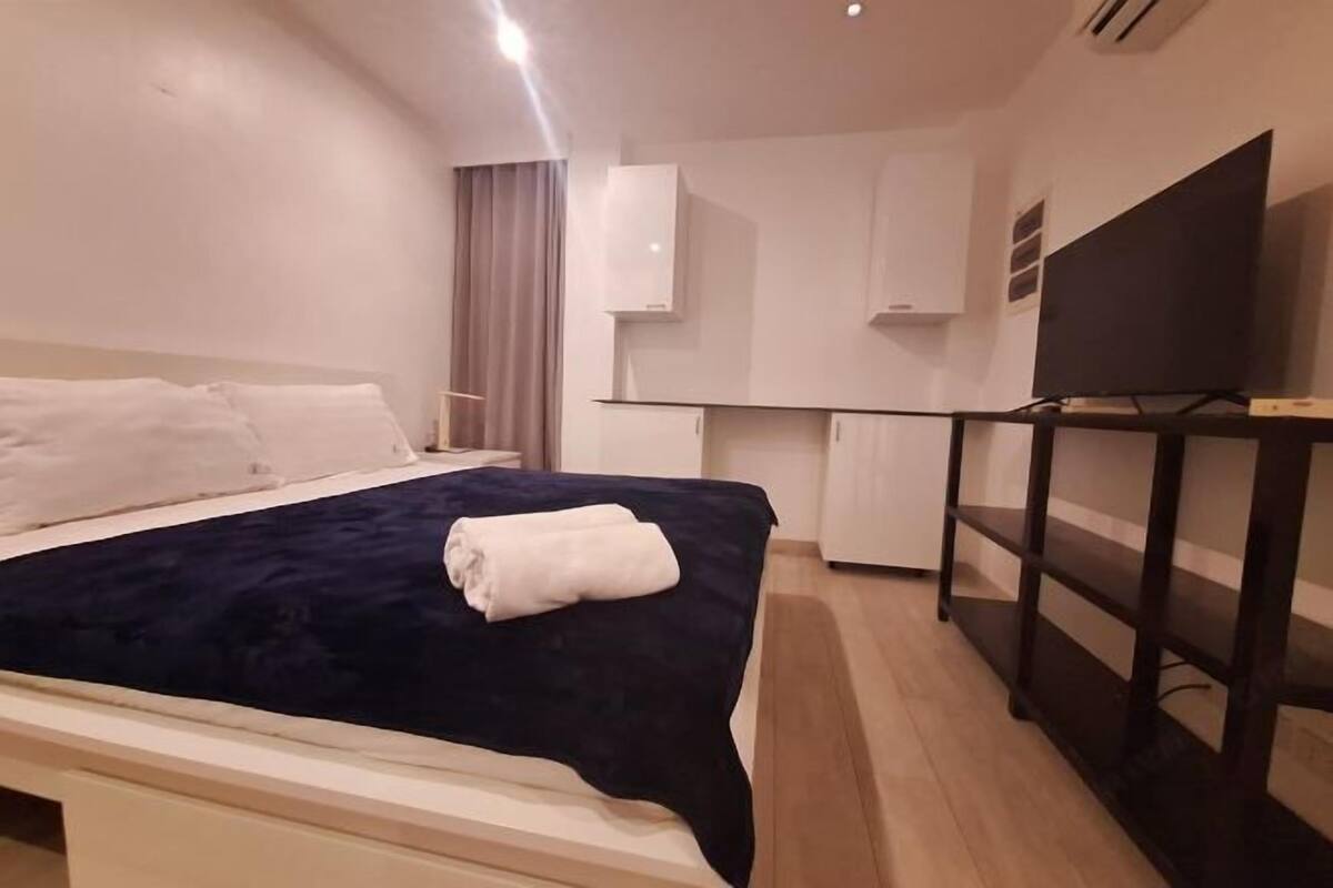 A hotel room with a bed, a desk, a TV, and a wardrobe.