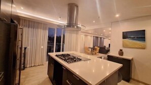 A modern kitchen with a central island, stainless steel range hood, and a dining area with a table and chairs. - Spacious 2BR Boracay Luxury Condo (Boracay Island)