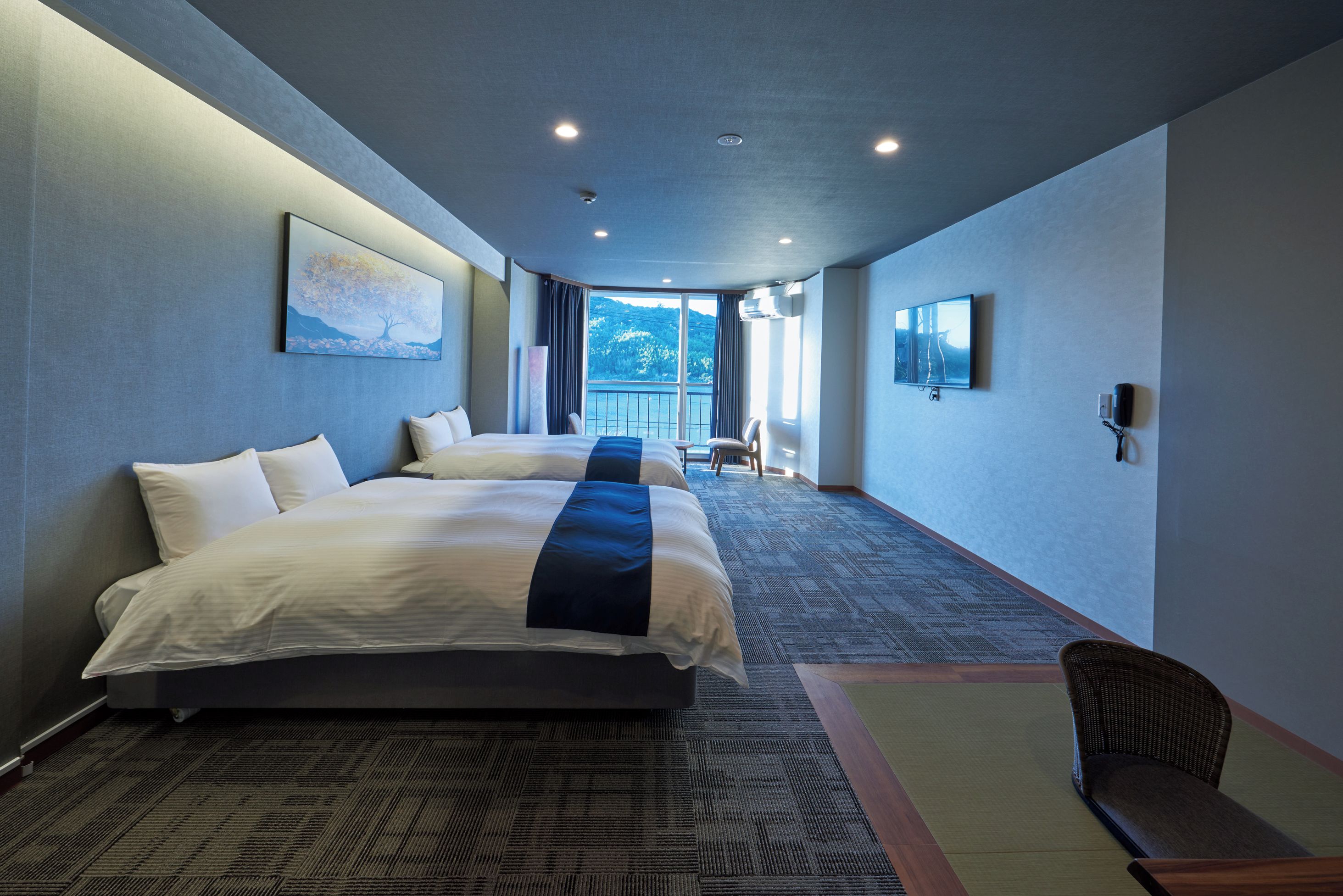 Ein Hotelzimmer mit zwei Betten, einem großen Fenster und Blick ins Freie.