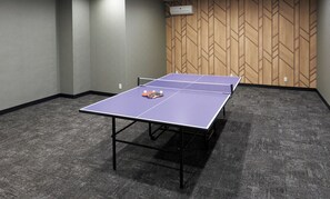 Ett bordtennisbord med bollar och racketar i ett rum med heltäckningsmatta på golvet och en vägg med ett mönster.