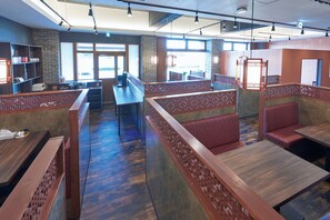En restaurang med höga träväggar som avgränsar olika områden, en bardisk och sittplatser i form av bås och bord.