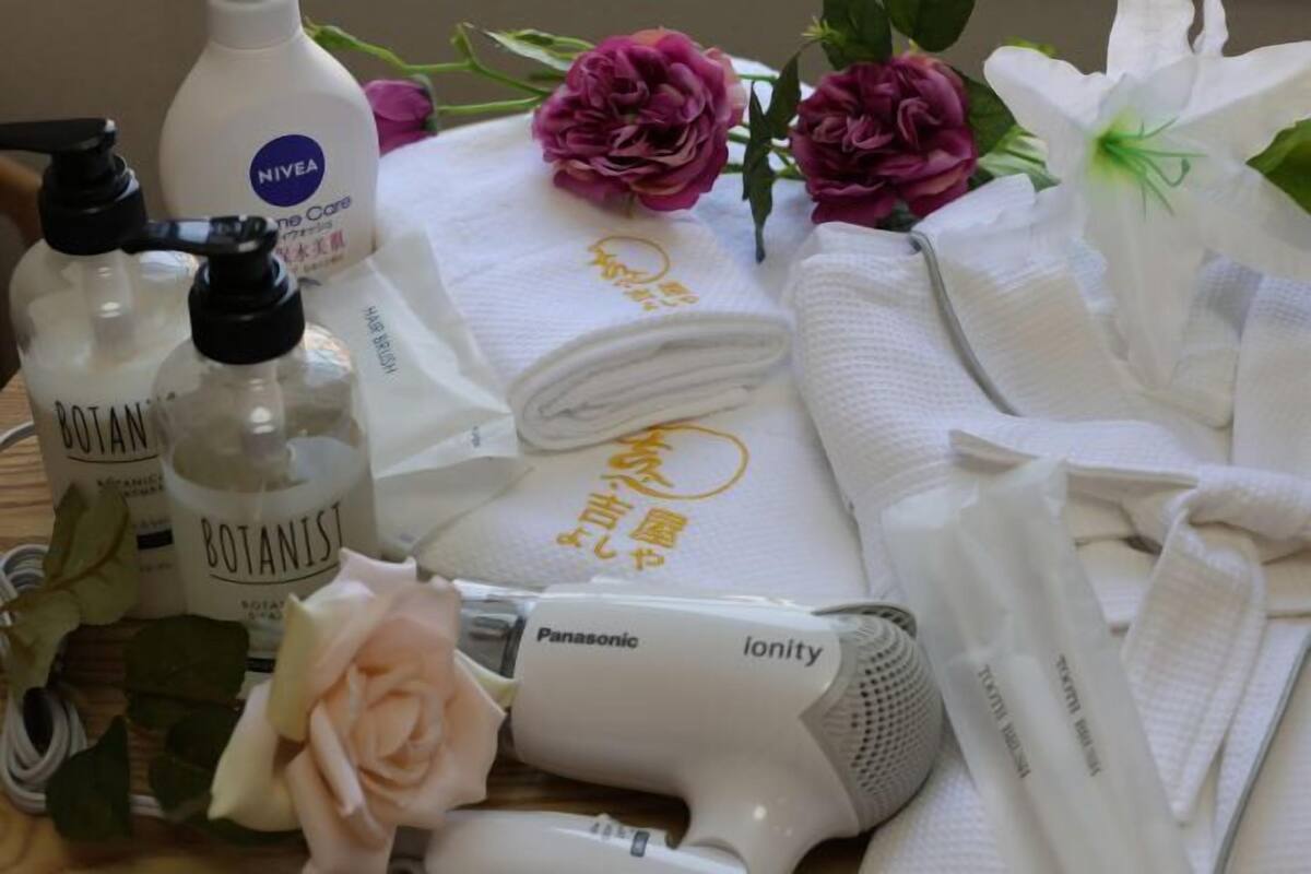 A bathroom with a hairdryer, bottles of hair care products, towels, and decorative flowers.
