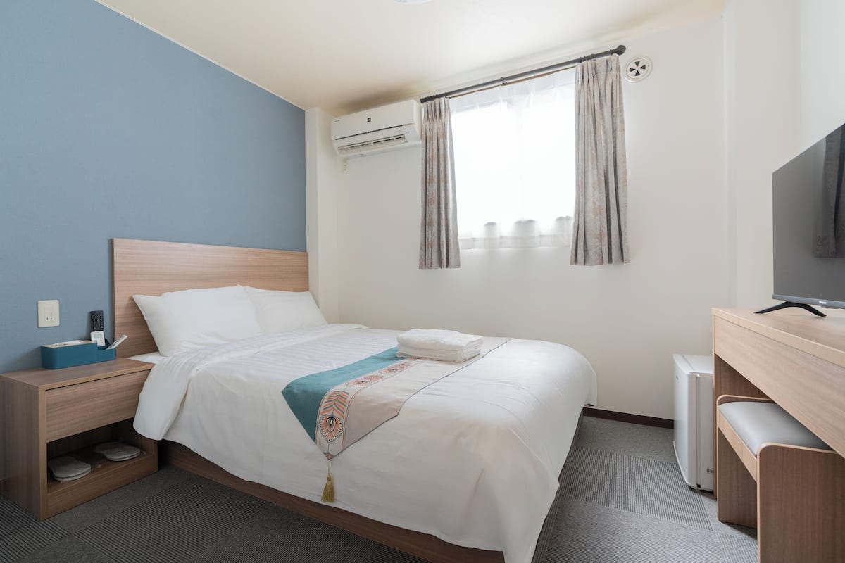 Habitación de hotel con cama, escritorio con televisor, aire acondicionado y ventana con cortinas.