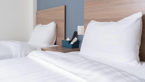 Habitación de hotel con dos camas, cabeceros de madera, ropa de cama blanca, una mesita de noche con una caja de pañuelos y un control remoto.