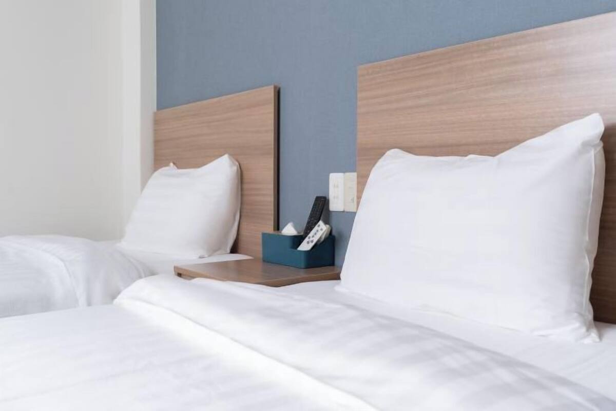 A hotel room with two beds, wooden headboards, white bedding, a bedside table with a tissue box and remote control.