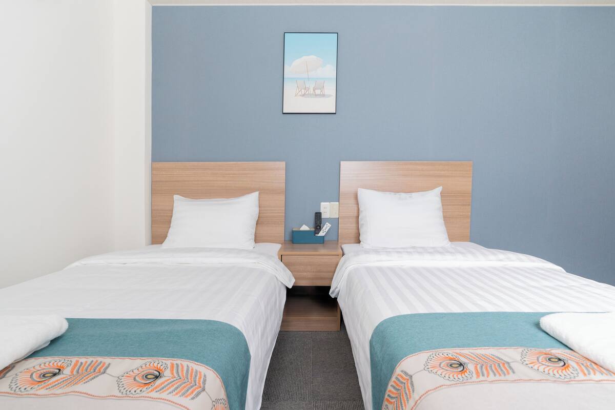 A hotel room with two beds, a nightstand with a remote control, and a framed picture on the wall.