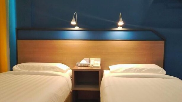 Habitación de hotel con dos camas, cabecero de madera, lámparas de noche y una mesita con teléfono y pañuelos.