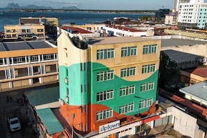 Un immeuble à plusieurs étages doté d’une façade colorée, d’une devanture visible avec une enseigne, et offrant une vue sur la mer en arrière-plan.