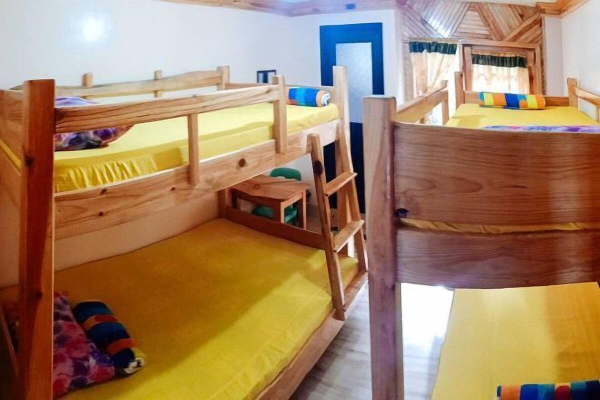 A bunk bed room with wooden railings, a door, and a window with curtains.