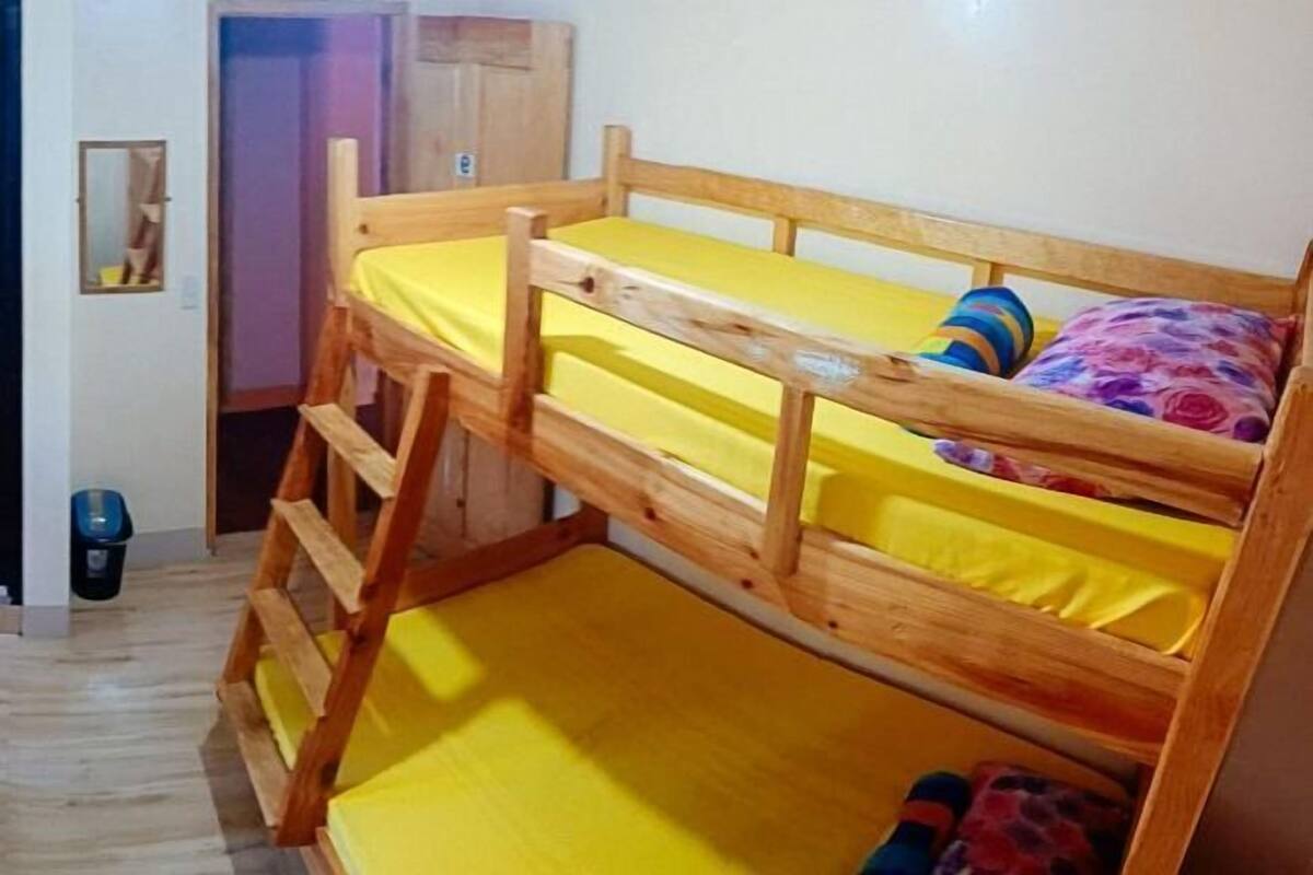 A bunk bed with yellow bedding, a wooden ladder, and a small mirror on the wall.