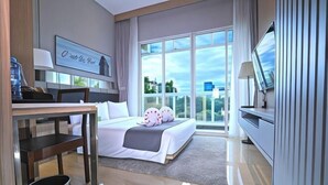Een moderne hotelkamer met een groot bed, een bureau, een televisie en uitzicht op de stad door grote ramen.