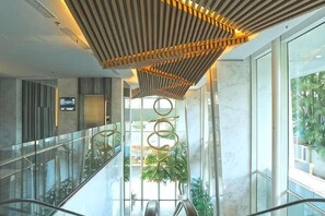 A modern interior with a glass railing, a central escalator, and a unique ceiling design. - Menteng Park Exclusive Emerald (Central Jakarta)