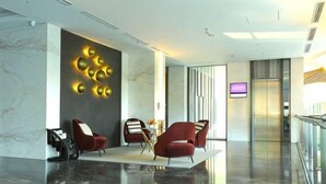 Een moderne lobby met een marmeren vloer, rode fauteuils, een wandlamp en een televisiescherm.