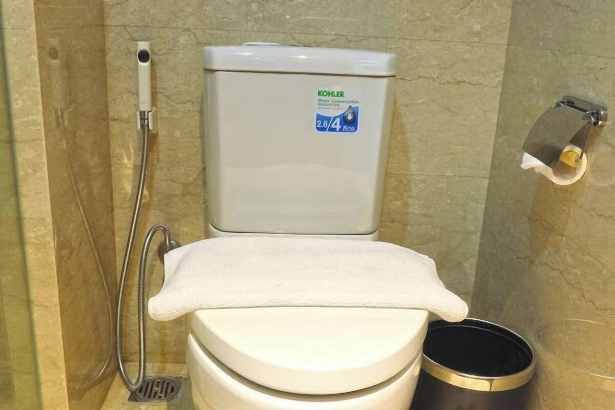 A toilet with a Kohler water conservation label, a handheld showerhead, and a trash can.